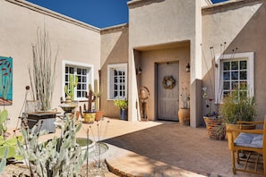A courtyard with cacti, a wooden chair, and a door with a wreath.