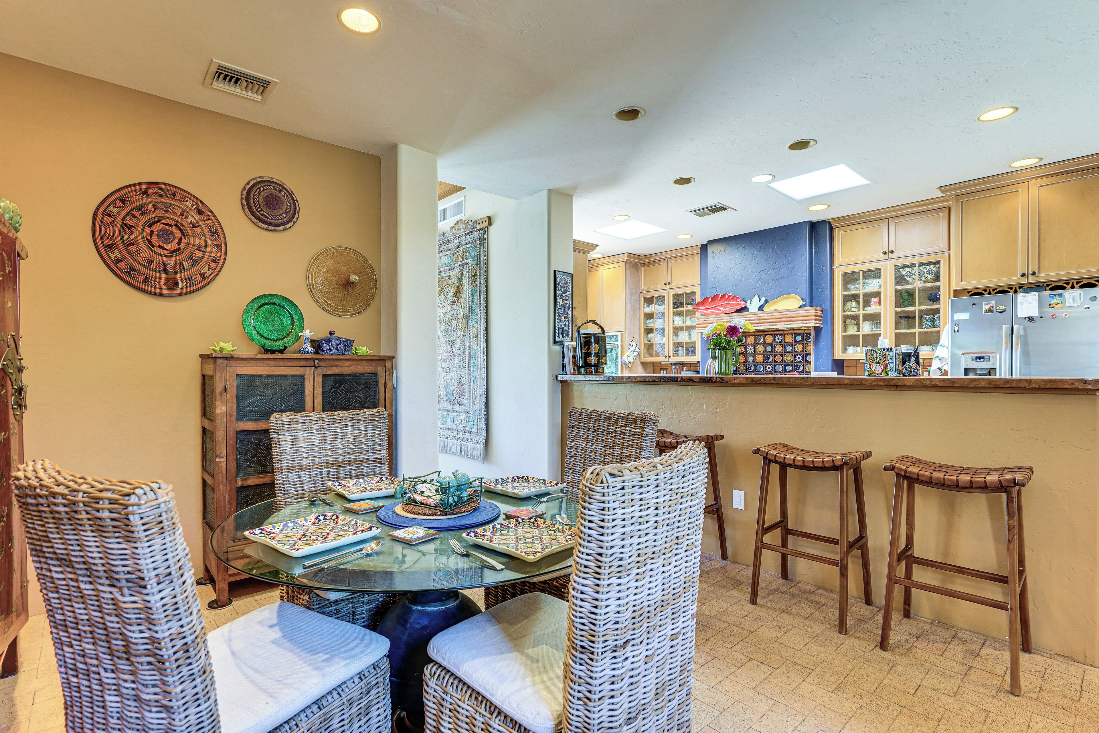 A dining area with wicker chairs, a glass table, and a kitchen in the background.