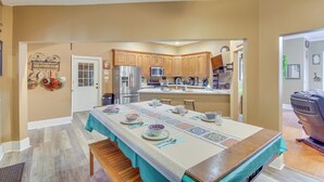 A kitchen with wooden cabinets, a stainless steel refrigerator, and a dining table set with plates and glasses. - Explore Gulf Coast & Beyond! Home w/ Yard & Games (Long Beach)