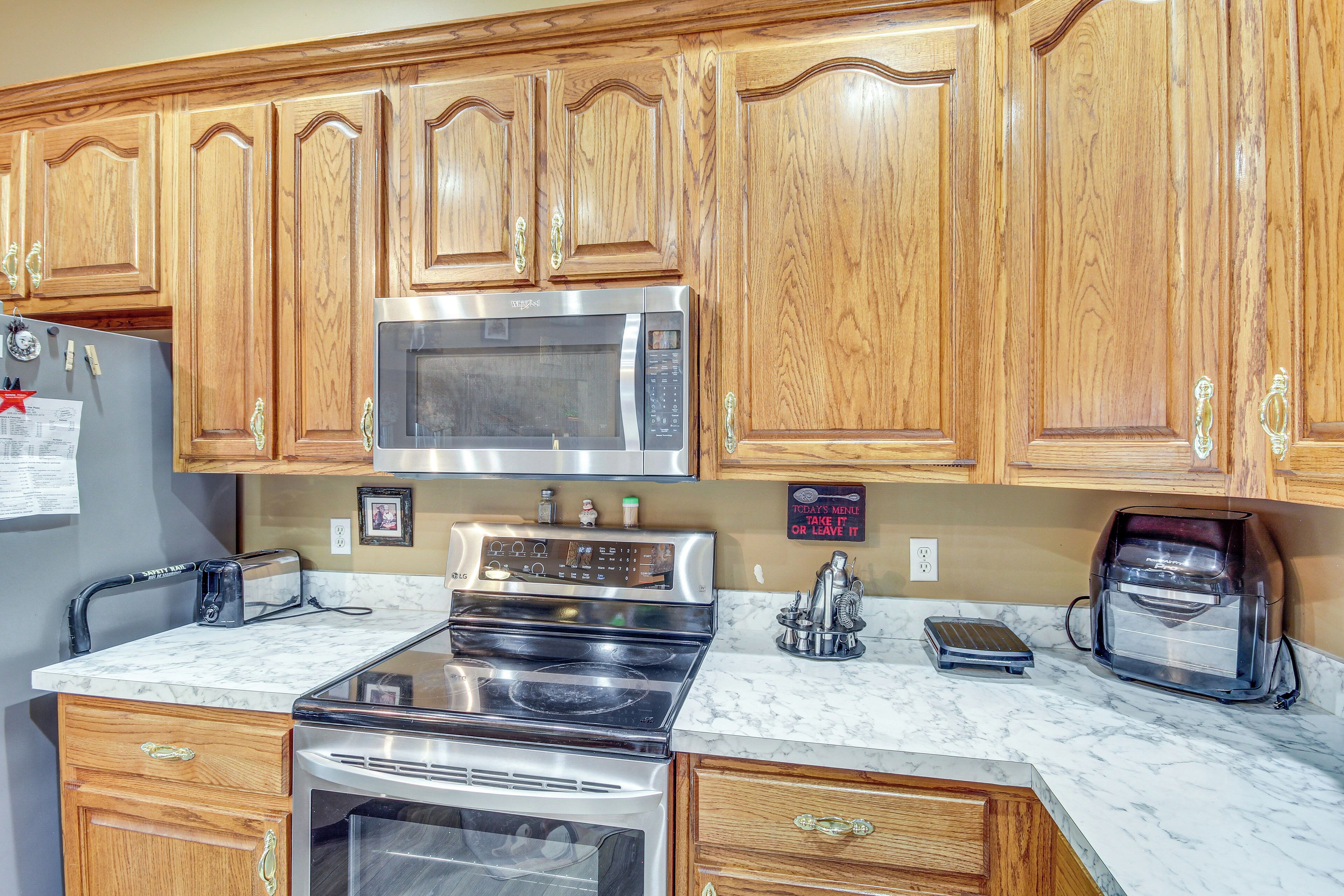 A kitchen with wooden cabinets, a stainless steel microwave, an oven, a toaster, and a coffee maker.