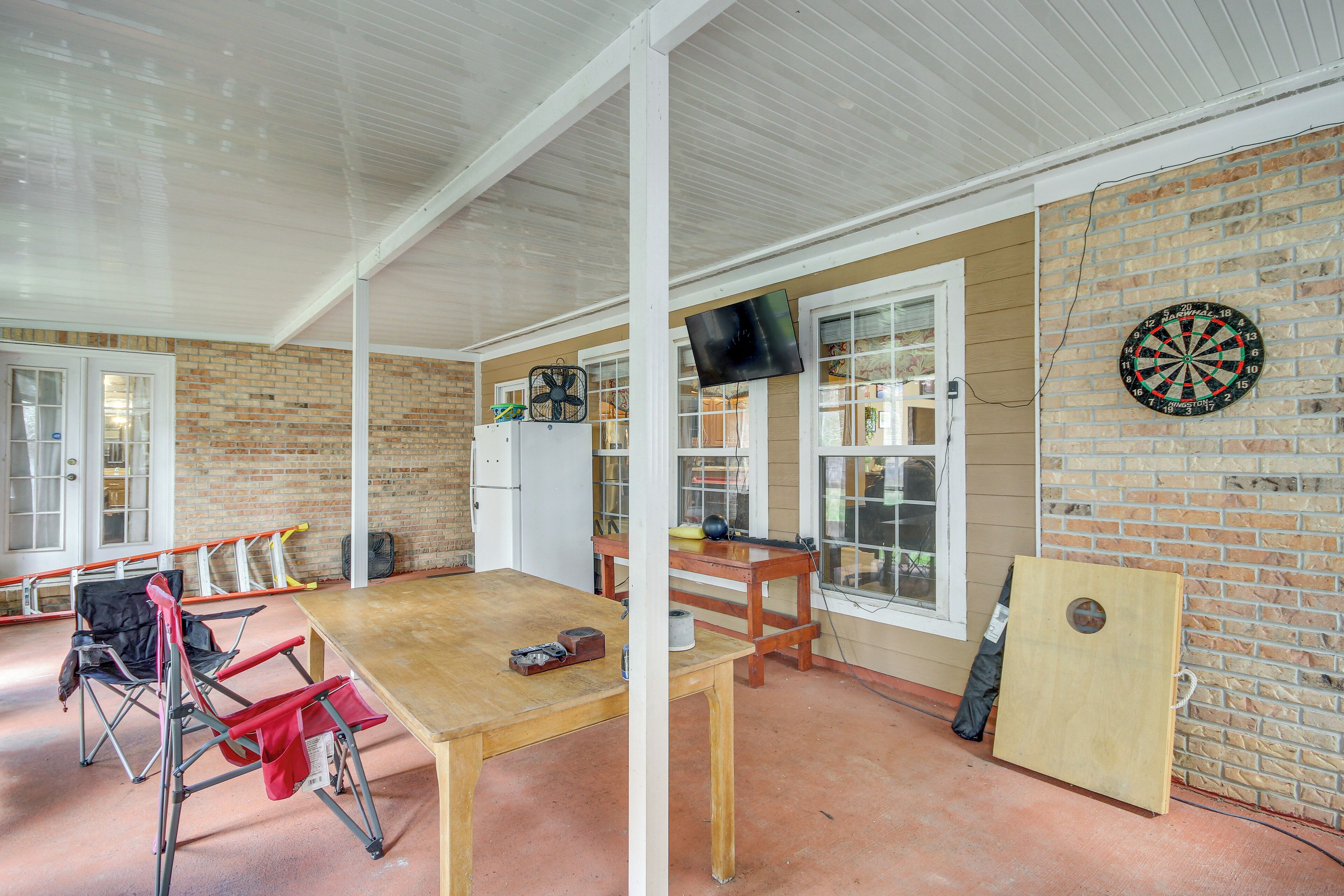 A room with a wooden table, a TV mounted on the wall, and a dartboard.