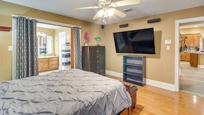 A bedroom with a bed, a ceiling fan, a TV, and a view into the kitchen. - Explore Gulf Coast & Beyond! Home w/ Yard & Games (Long Beach)