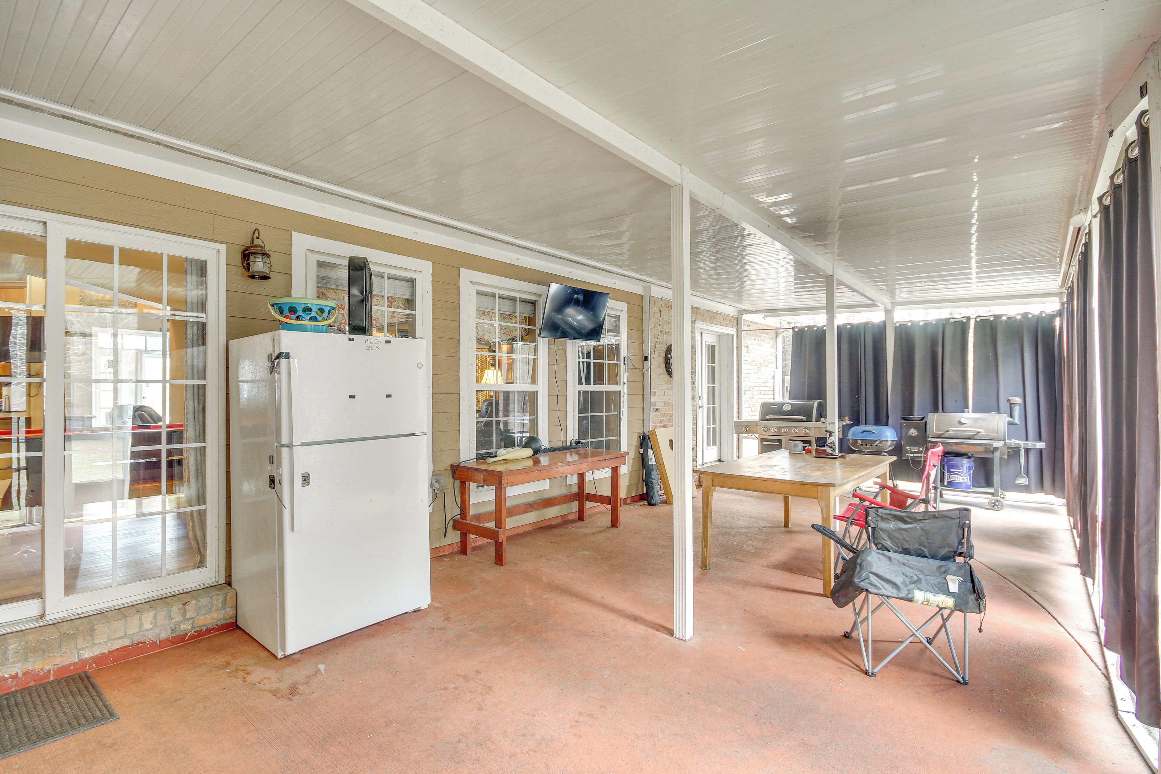 A covered patio area with a refrigerator, a table, and a grill.