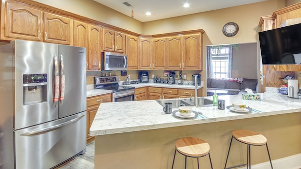 A kitchen with wooden cabinets, stainless steel appliances, a marble countertop, and a large island with stools. - Explore Gulf Coast & Beyond! Home w/ Yard & Games (Long Beach)