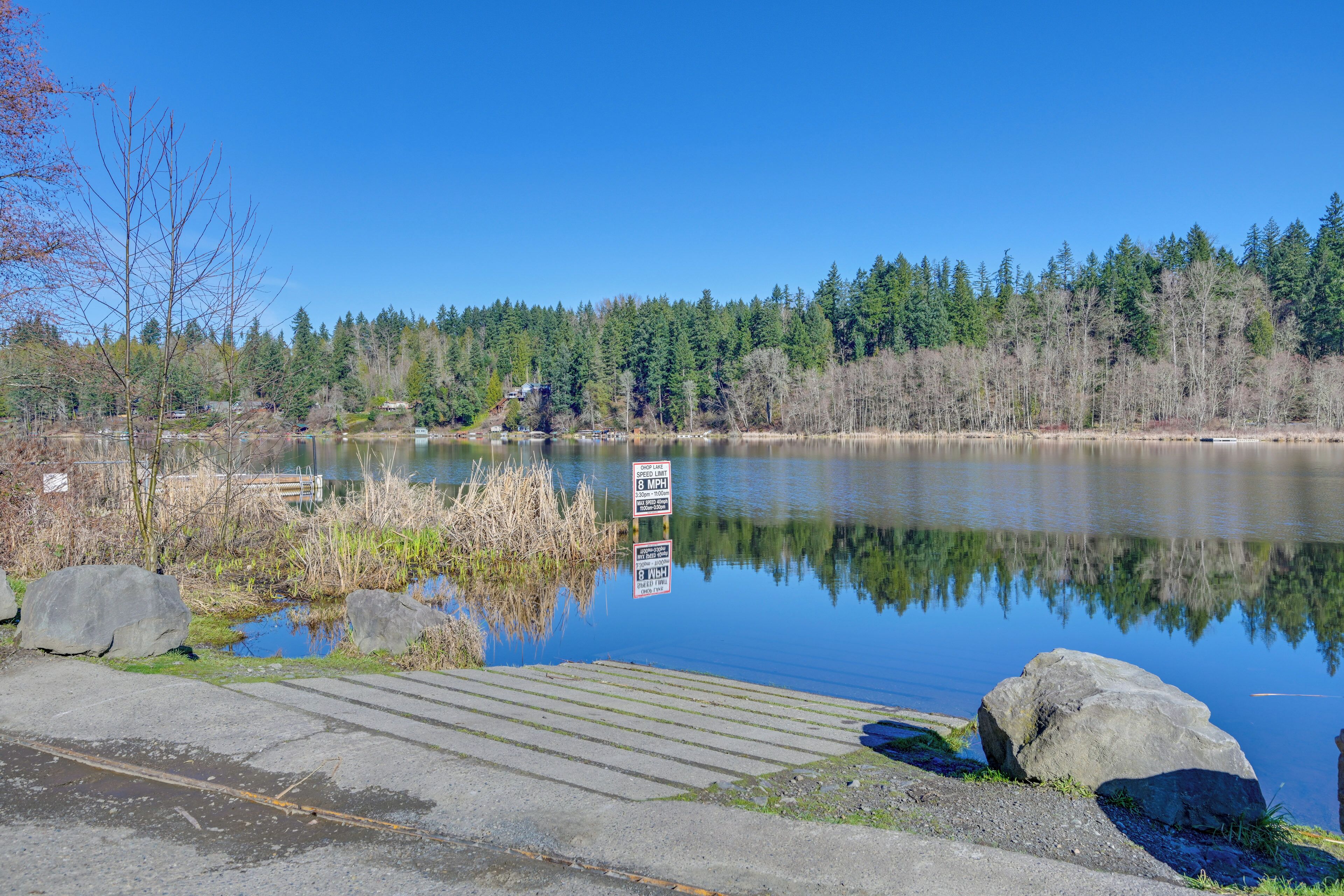 A calm lake with a dock, surrounded by trees and a clear sky.