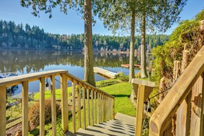 Una escalera de madera que conduce a una terraza junto al lago, con mobiliario exterior y vistas al lago y al bosque.