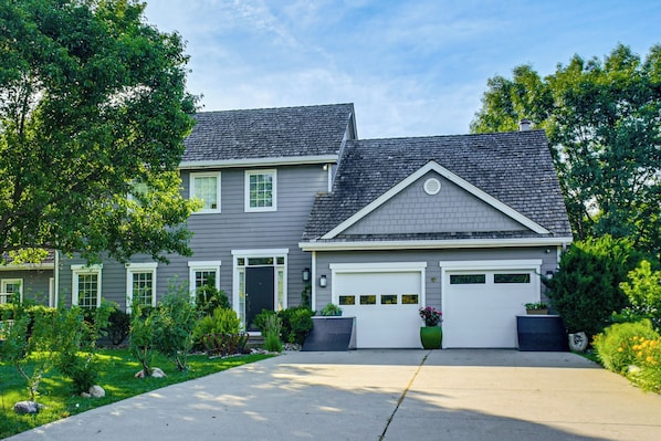 A two-story house with a garage, a front yard with landscaping, and a clear sky.