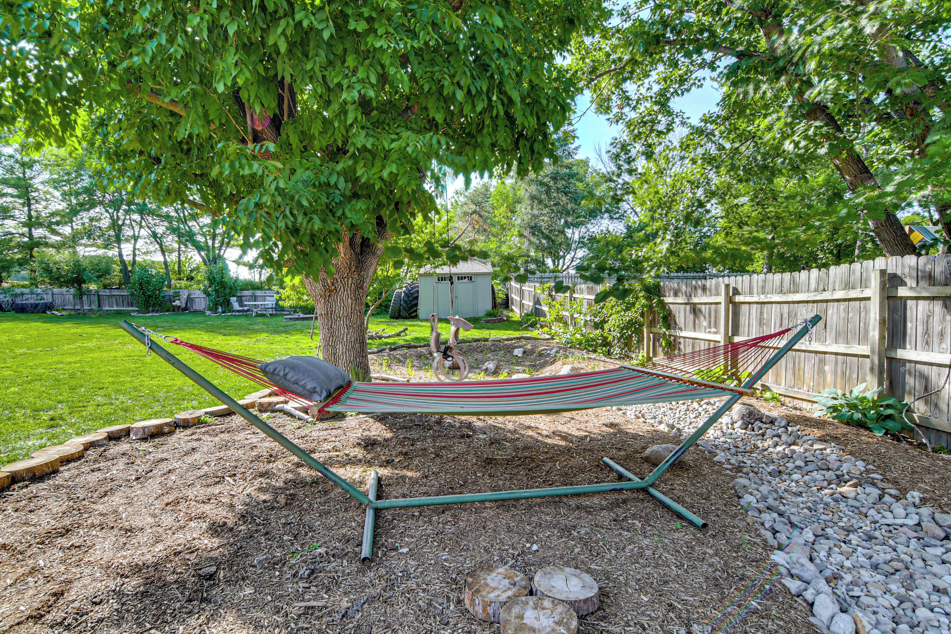 A hammock under a tree in a backyard with a wooden fence and a shed.
