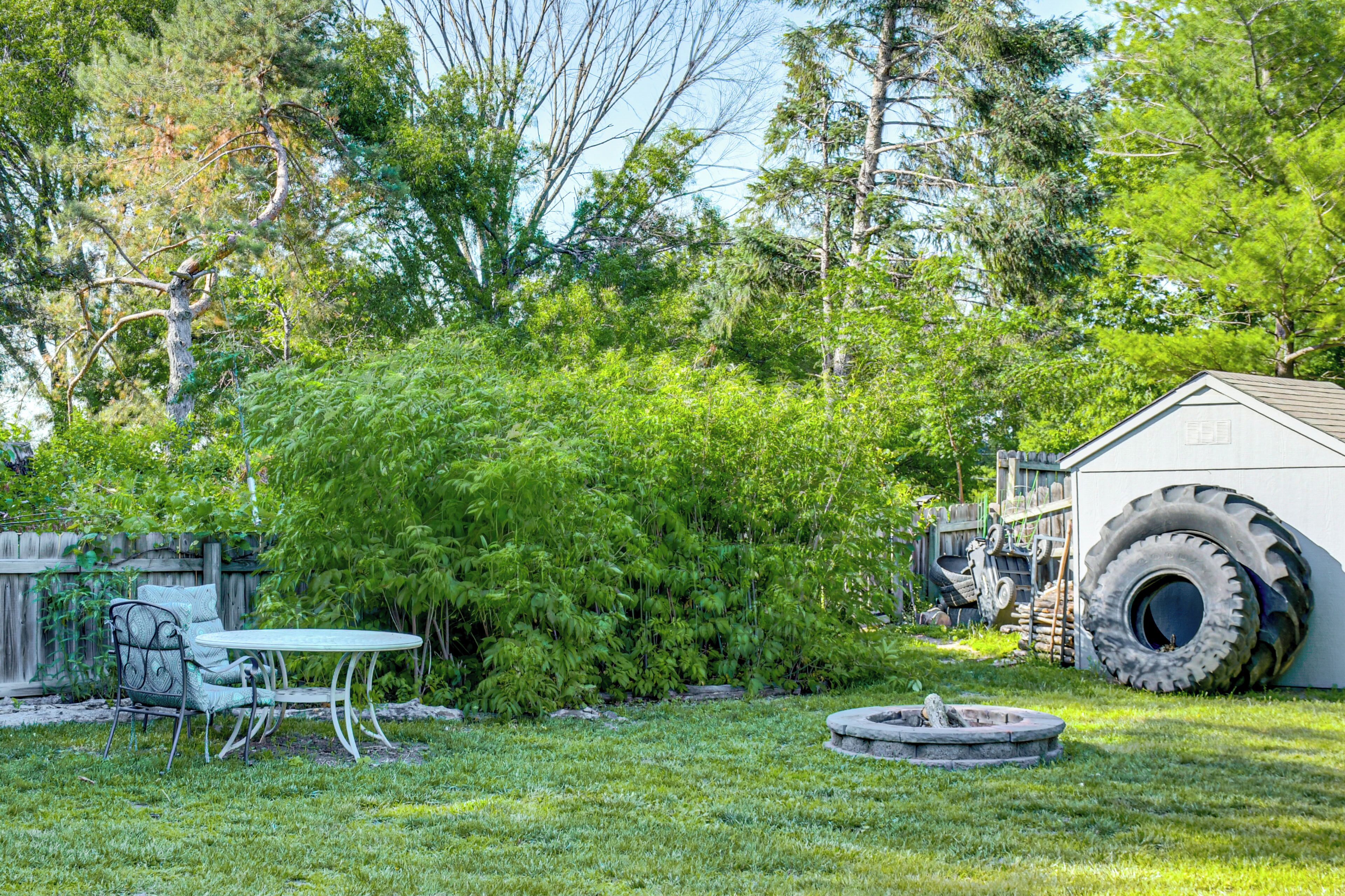 A backyard with a round table and chairs, a wooden fence, and a shed with large tires.
