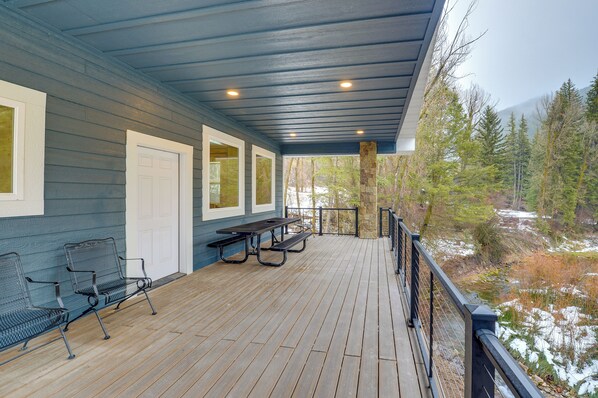 A covered deck with wooden flooring, metal chairs, and a picnic table.