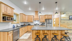 Une cuisine moderne avec des meubles en bois, des appareils en acier inoxydable, un grand îlot central avec des tabourets et un éclairage suspendu.