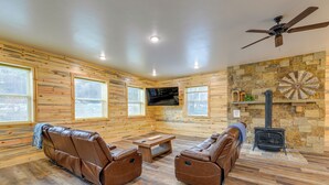 L’intérieur d’un chalet en rondins, avec des fauteuils inclinables en cuir, une cheminée en pierre et un téléviseur fixé au mur.