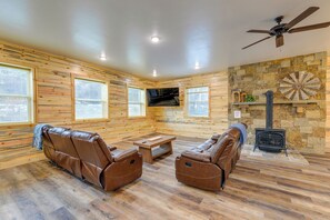 A log cabin interior with leather recliners, a stone fireplace, and a television mounted on the wall. - Mountain Retreat By the River: Star Valley Getaway (Afton)