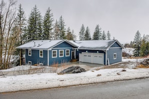 Ein blaues, zweistöckiges Haus mit Garage, umgeben von schneebedecktem Boden und Bäumen.
