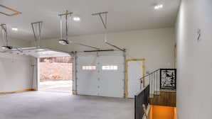 Un grand garage doté d’une large porte blanche, d’un escalier en bois et d’une structure métallique au plafond.