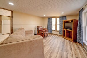 Una sala de estar con un sofá, un mueble de madera con televisor, una silla y una pequeña mesa.