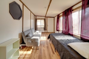 Une chambre moderne avec un plancher en bois, un canapé gris, un lit avec une couette grise et une fenêtre avec des rideaux rouges.