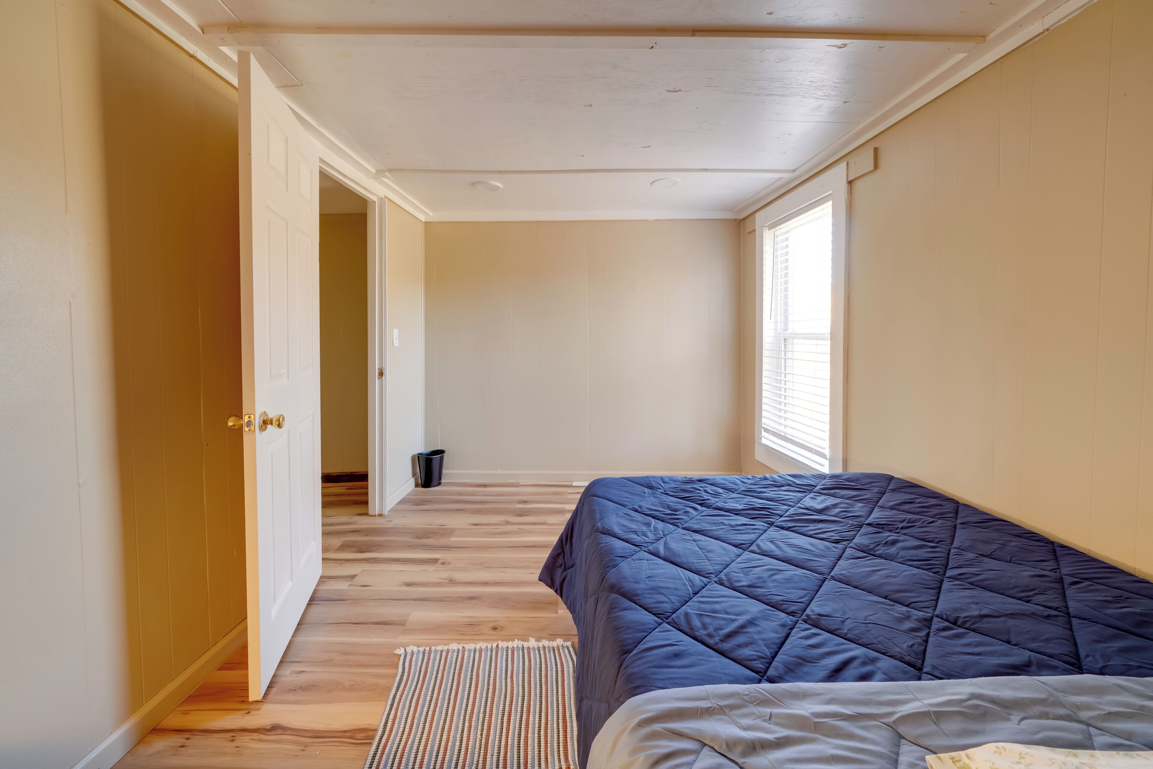 Ein Schlafzimmer mit Bett, Holzboden, einer Tür und einem Fenster.