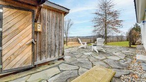 A wooden shed with a stone patio, two Adirondack chairs, and a view of the countryside. - Hike, Bike, & Explore: Vermont Family Farmhouse! (New Haven)