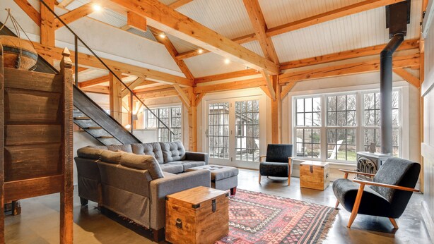 A spacious living area with a wooden staircase, a sofa set, a patterned rug, and a large window. - Hike, Bike, & Explore: Vermont Family Farmhouse! (New Haven)