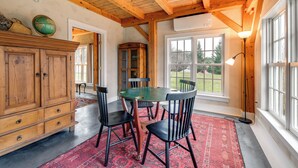 A dining area with a wooden table and chairs, a red patterned rug, and a large window with a view of the outdoors. - Hike, Bike, & Explore: Vermont Family Farmhouse! (New Haven)