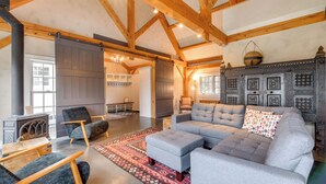 A spacious living room with a large grey sectional sofa, a fireplace, and a rustic wooden ceiling. - Hike, Bike, & Explore: Vermont Family Farmhouse! (New Haven)