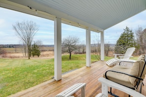 A covered porch with wooden flooring, white columns, and two Adirondack chairs.
