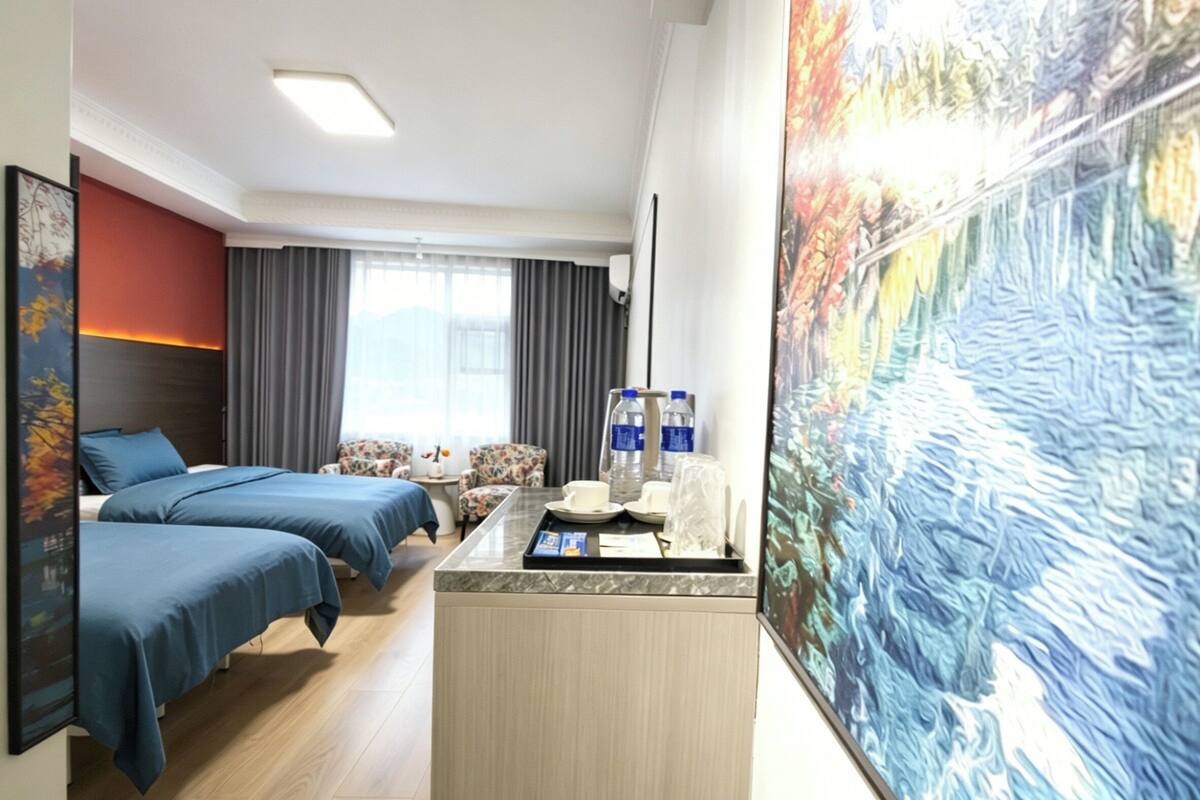 A hotel room with two beds, a desk with a computer, a window with curtains, and a large painting on the wall.