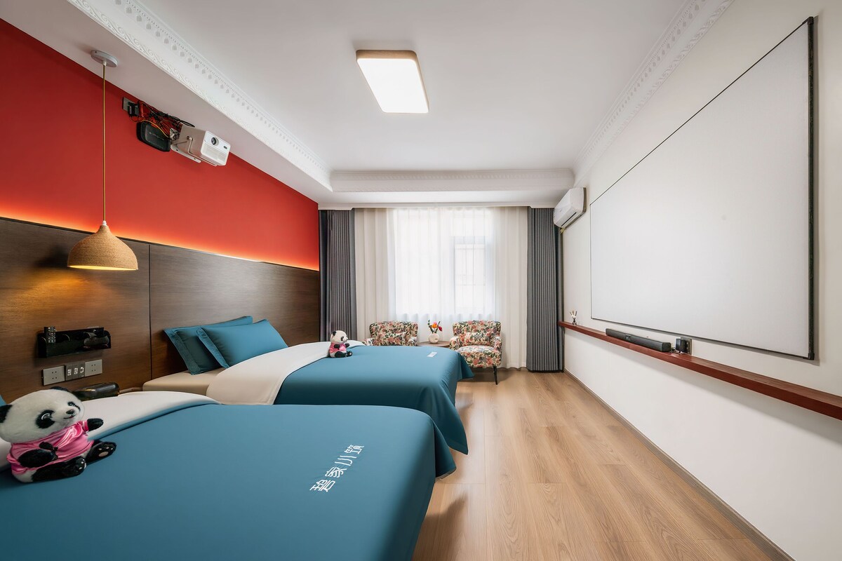 Une chambre d’hôtel avec deux lits, un bureau, une chaise, une fenêtre avec des rideaux et un écran de projection.