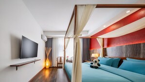 Habitación de hotel con cama, televisión montada en la pared, mesita de noche con lámpara y ventana con cortinas.