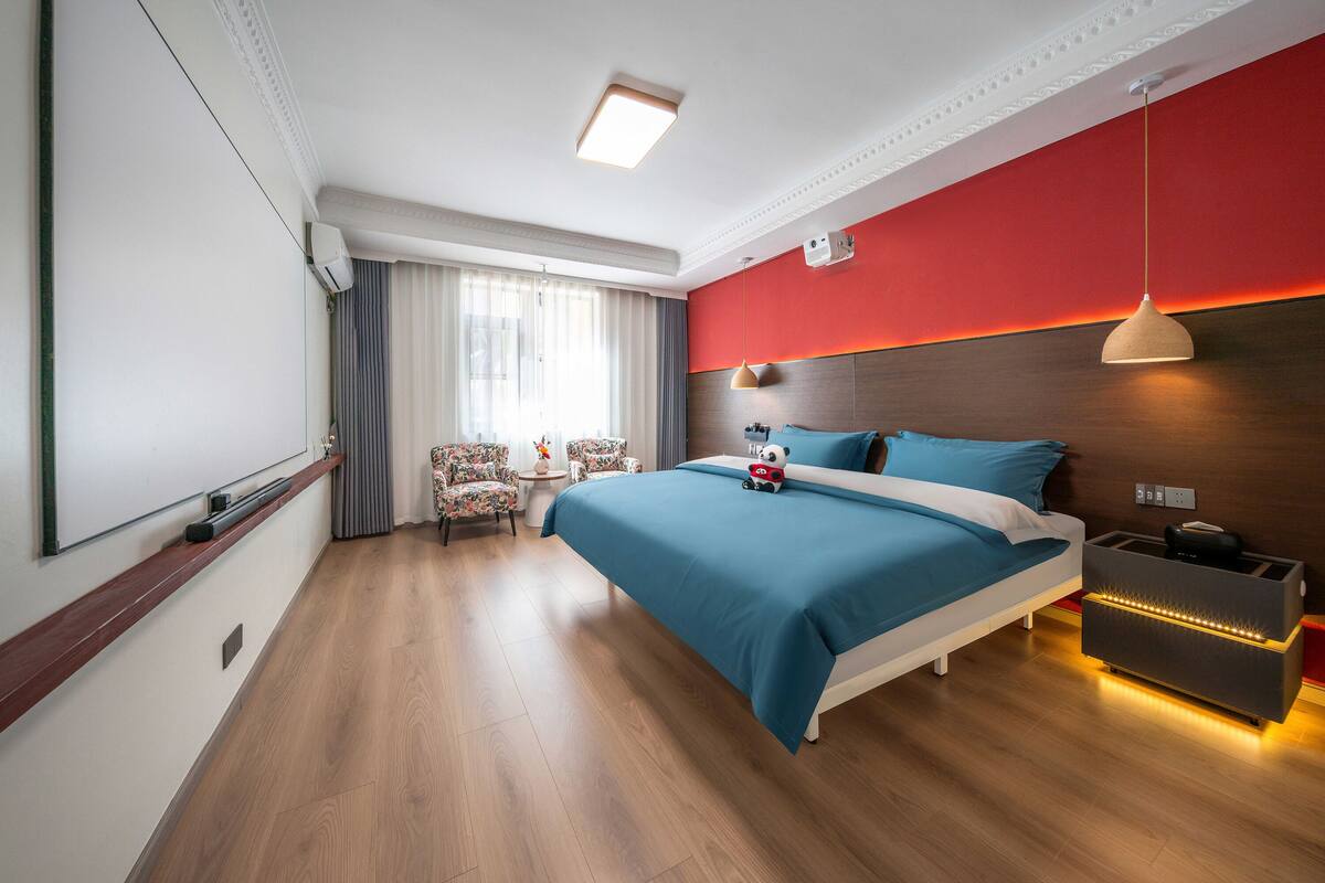 A modern hotel room with a large bed, a desk, and a seating area with two chairs.