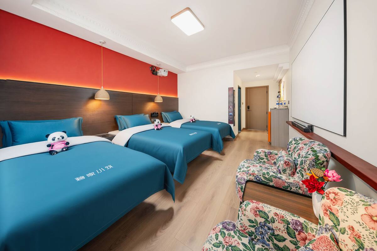 A hotel room with two beds, a sofa, a TV, and a red accent wall.
