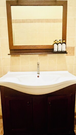 A bathroom with a white sink, a mirror above it, and a shelf with toiletries. - Mara Villa Katunayake - 5 Mins to Colombo Airport (Seeduwa - Katunayake)