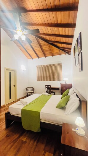 A bedroom with a wooden ceiling, a bed with a green bedspread, two chairs, a desk, and a nightstand with a lamp. - Mara Villa Katunayake - 5 Mins to Colombo Airport (Seeduwa - Katunayake)