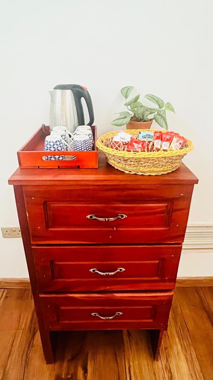 A wooden chest of drawers with a kettle, patterned containers, and a basket with items on top.