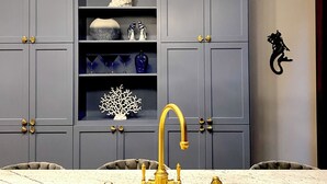 A modern kitchen with grey cabinets, a white marble countertop, and gold fixtures.