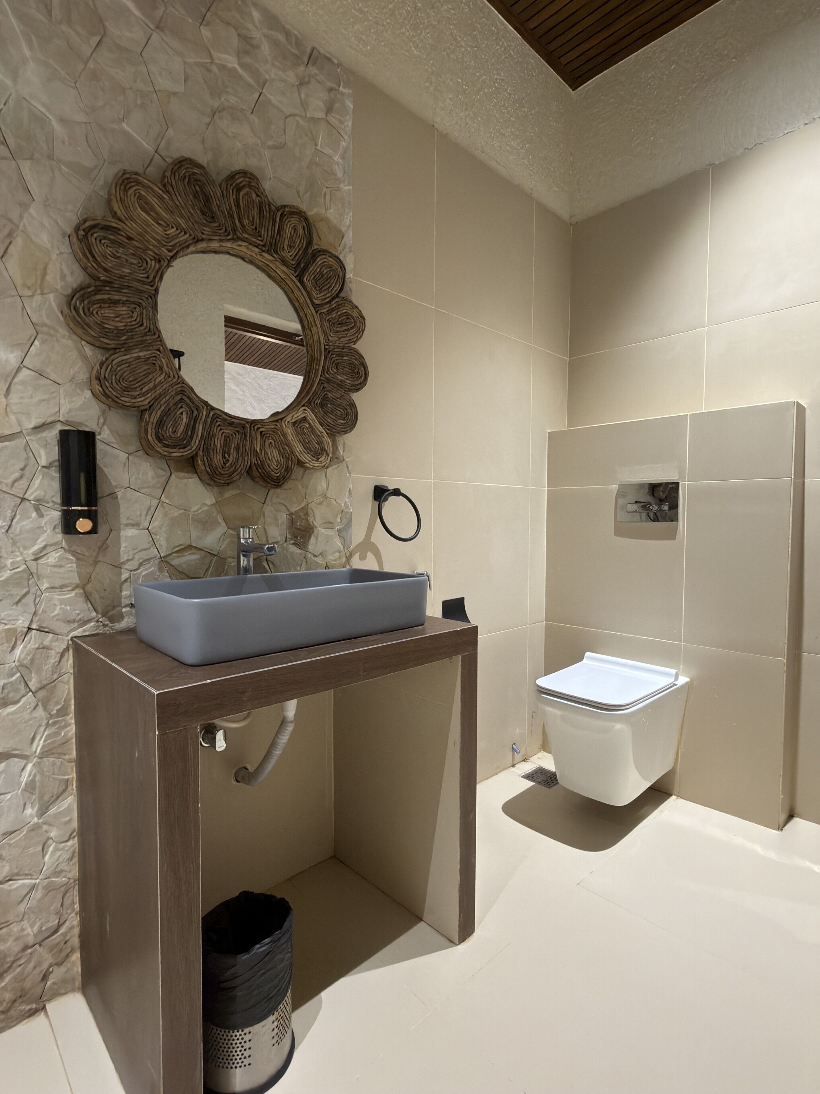 A bathroom with a stone wall, a wooden vanity with a sink, a mirror, and a toilet.
