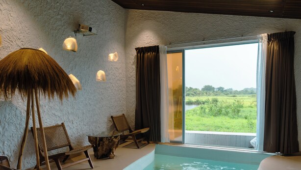 A room with a pool, a chair, a table, and a large window with curtains. - Hidden Beach Resort by Greenleaf Aqua (Karjat)