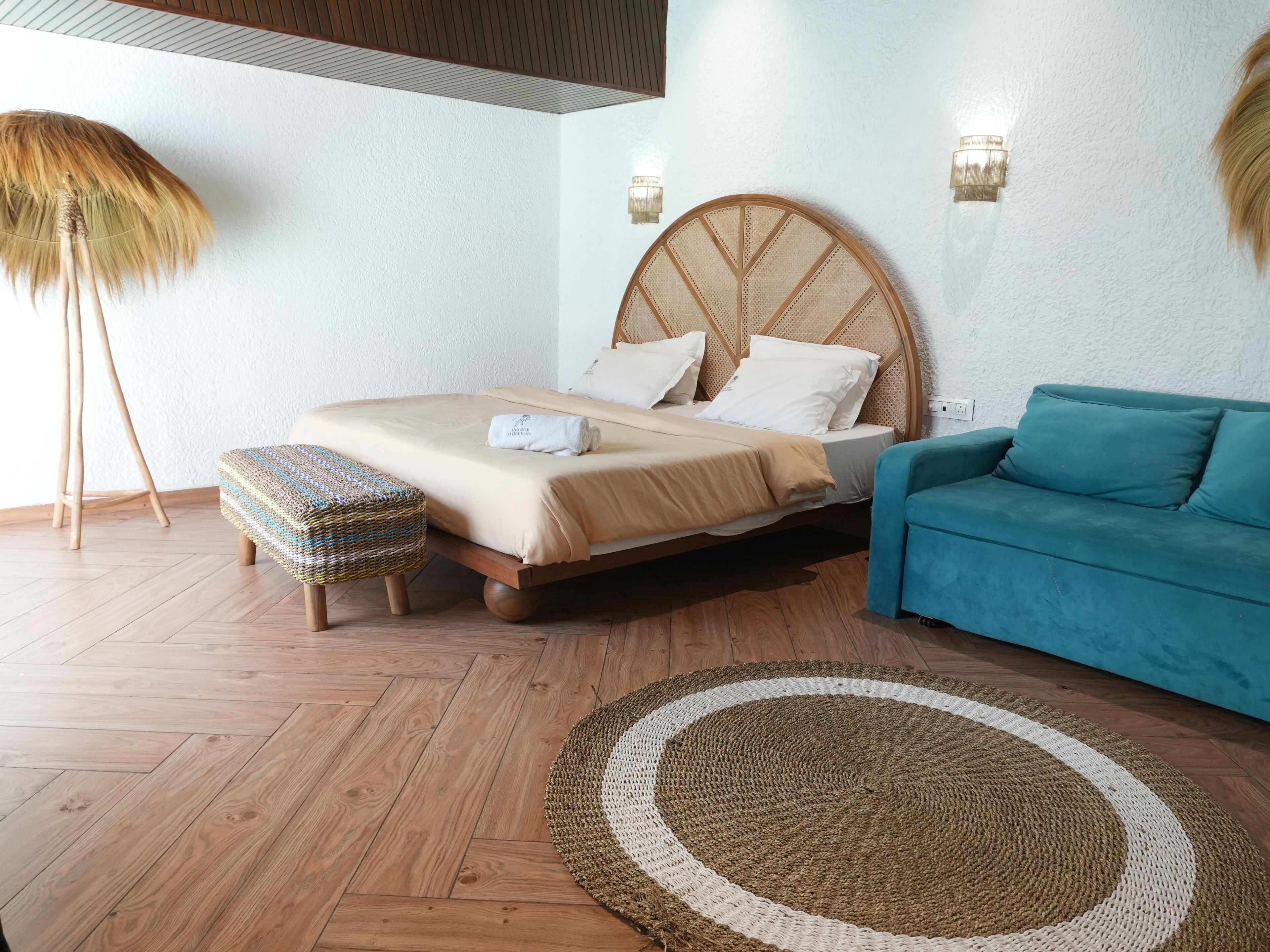 A bedroom with a wooden bed, a blue sofa, a woven ottoman, and a round rug.