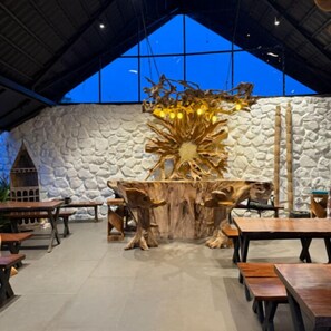 A restaurant interior with stone walls, wooden tables, and a large tree sculpture centerpiece. - Hidden Beach Resort by Greenleaf Aqua (Karjat)