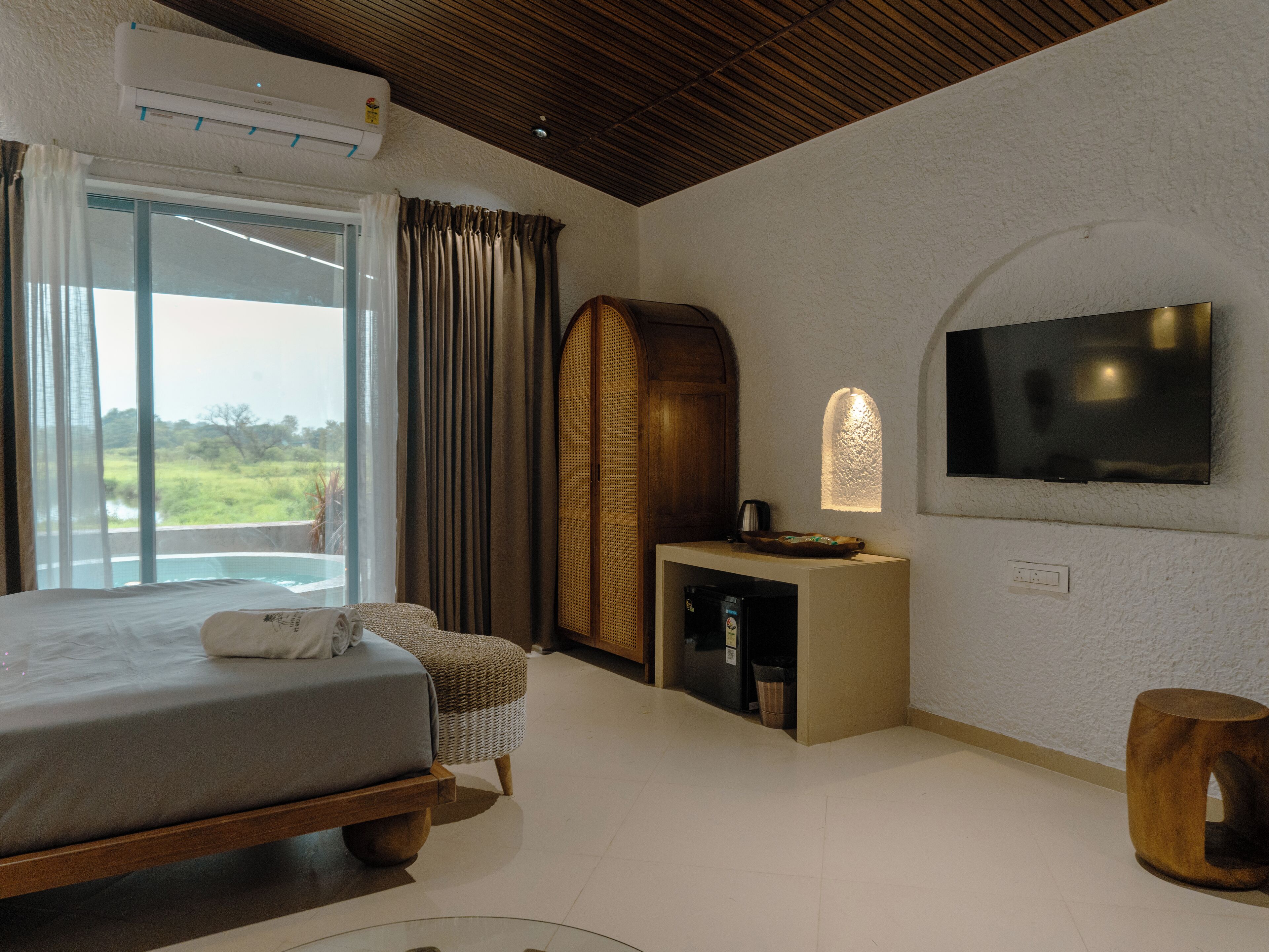 A modern hotel room with a large bed, a television, a small table, and a view of the outdoors.