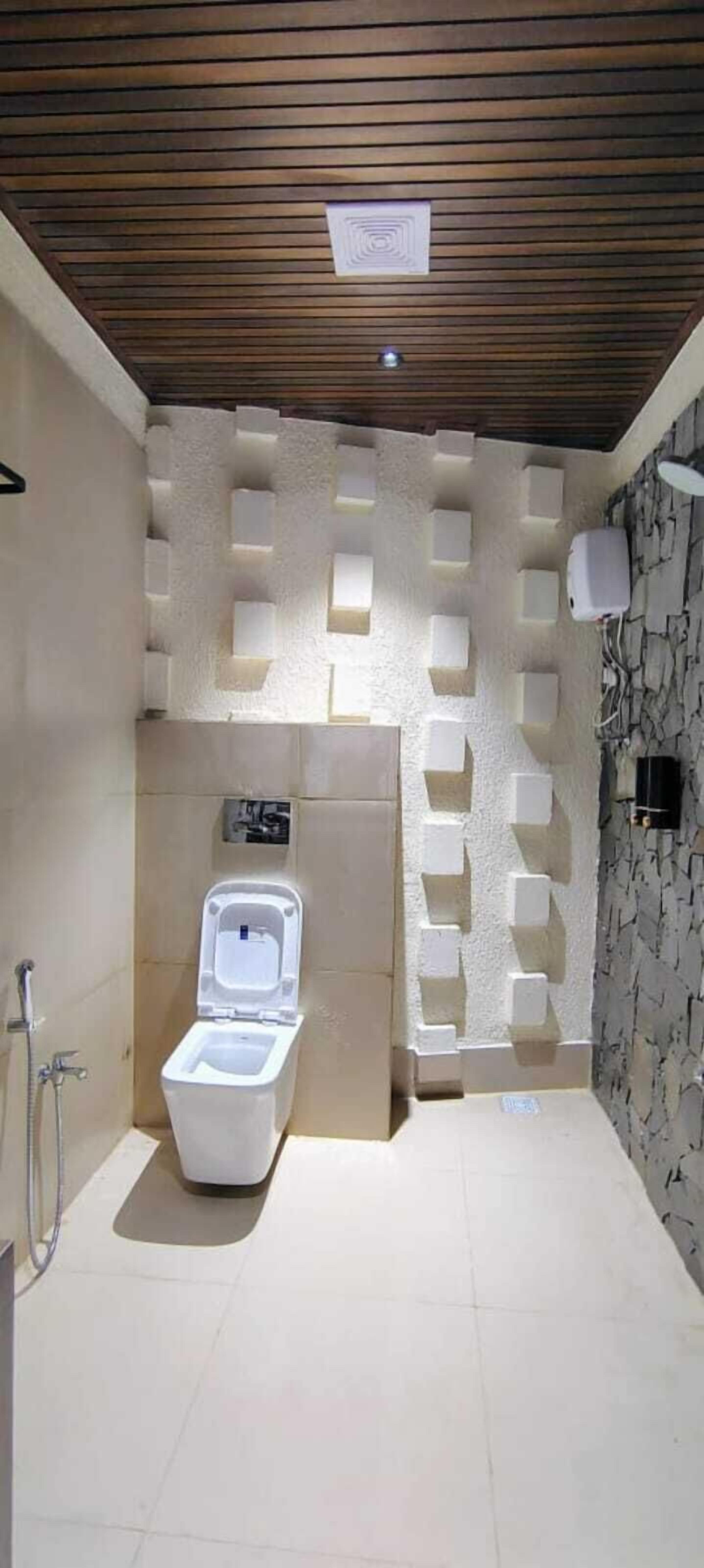 A modern bathroom with a white toilet, a shower area, and a textured wall design.