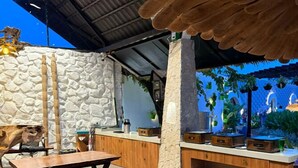 A restaurant with wooden tables and benches, stone walls, and hanging plants. - Hidden Beach Resort by Greenleaf Aqua (Karjat)