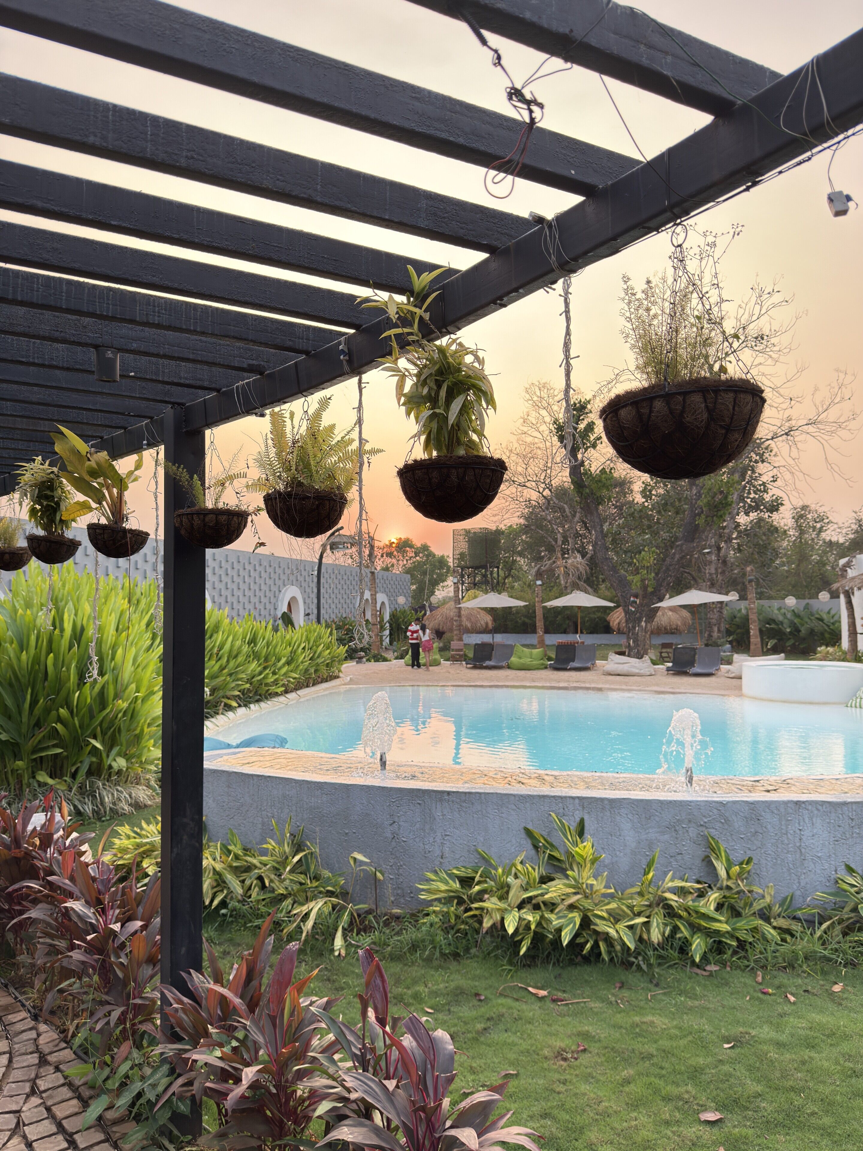 Un espace piscine agrémenté de jardinières suspendues, d’une fontaine et de chaises longues.
