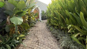 A paved pathway flanked by lush green plants and a brick wall with a geometric pattern. - Hidden Beach Resort by Greenleaf Aqua (Karjat)