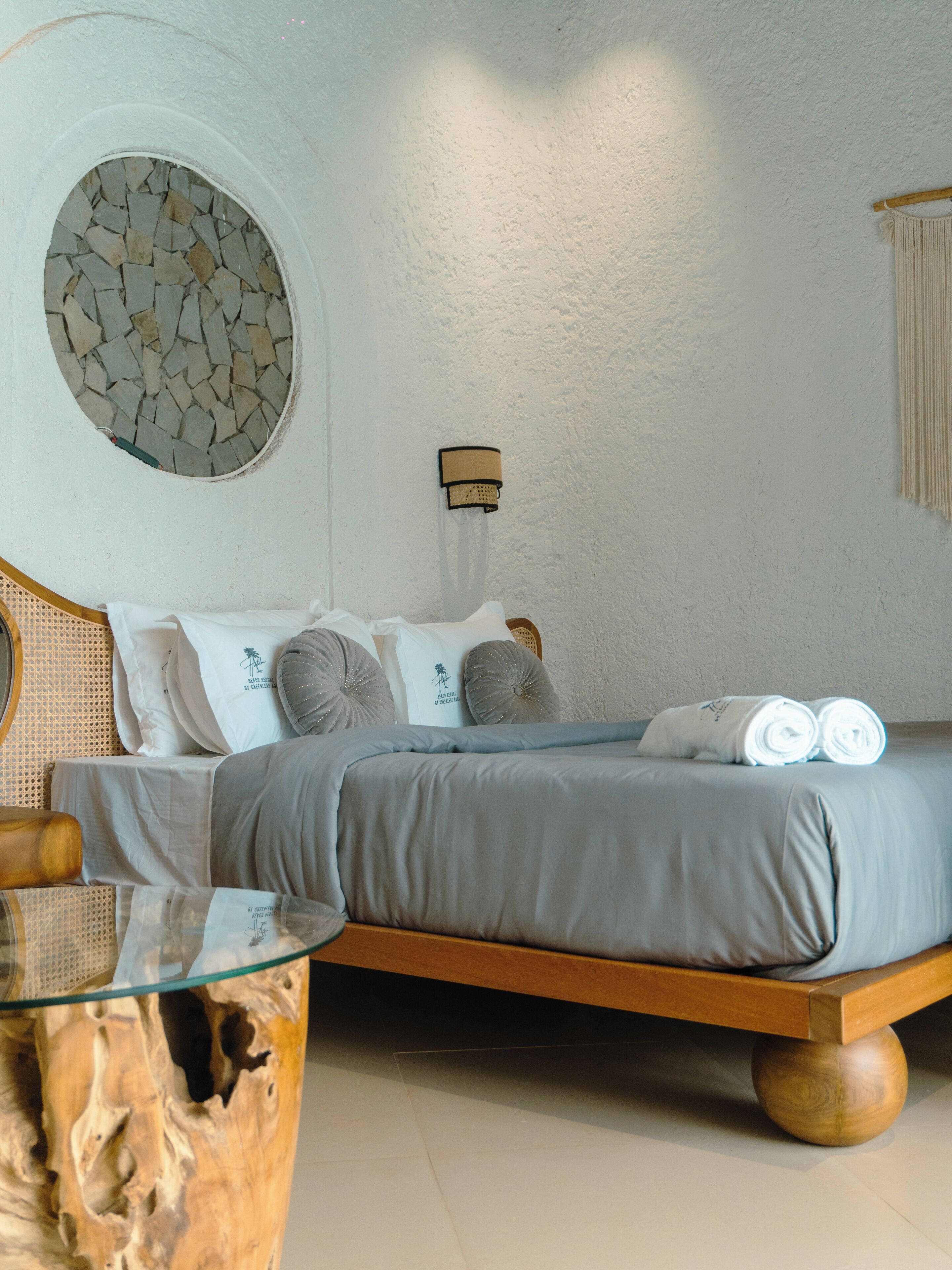 Une chambre à coucher avec un lit, des oreillers, une lampe fixée au mur et un élément décoratif en pierre circulaire sur un des murs.