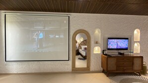 A room with a large projection screen, a television, a wooden cabinet, and a mirror. - Hidden Beach Resort by Greenleaf Aqua (Karjat)