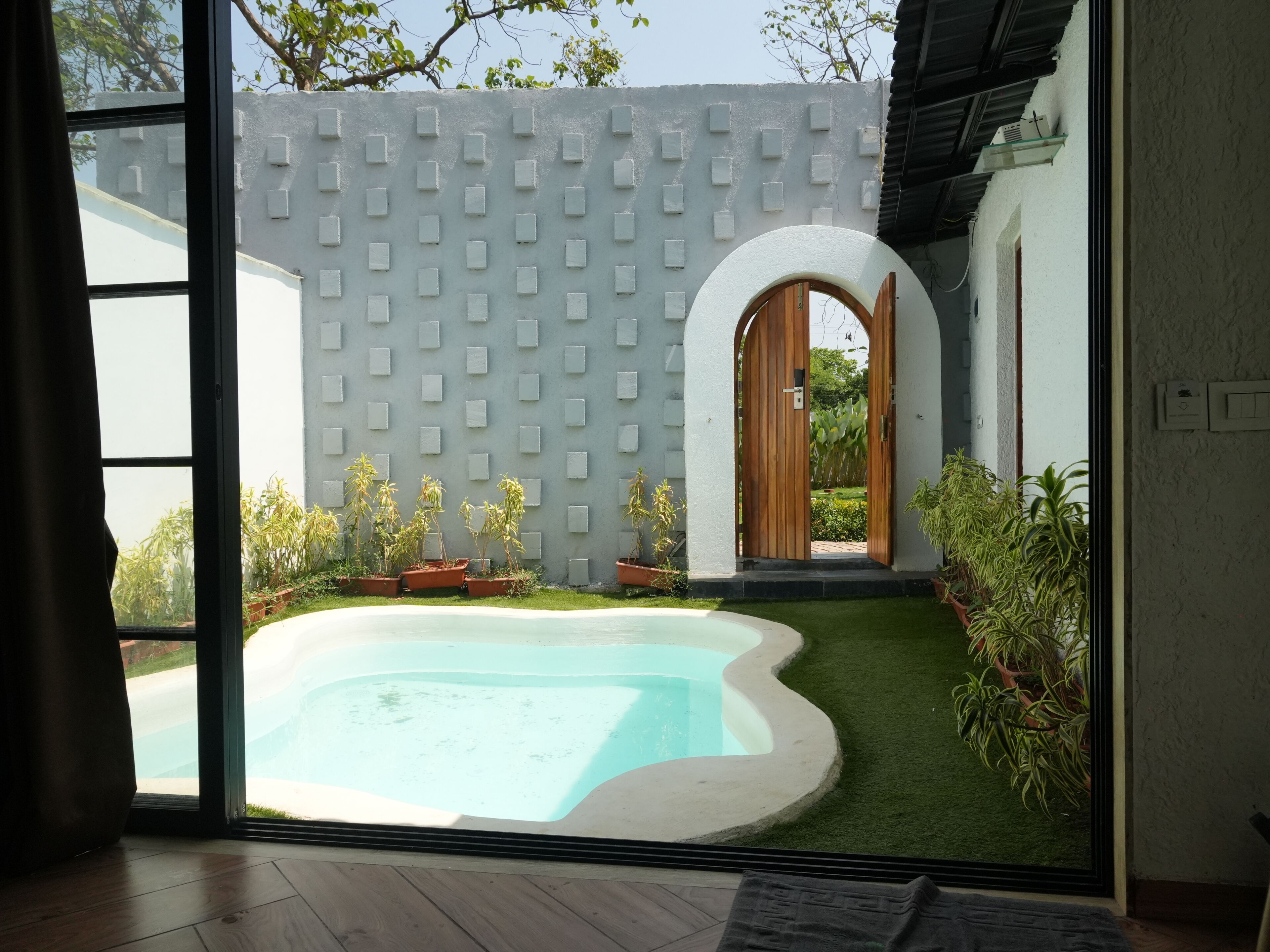 A modern indoor pool area with a clear view of the surrounding garden and a wooden door leading outside.