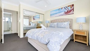 A hotel room with a large bed, a bathroom with a glass shower, and a beach-themed painting on the wall. - The Wharfside Oasis by the Waves (Surfers Paradise)