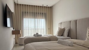 Una habitación de hotel moderna con una cama grande, otra más pequeña, un televisor de pantalla plana en la pared y un ventanal con cortinas traslúcidas.